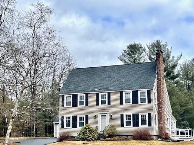 colonial-style house featuring a chimney and roof with shingles