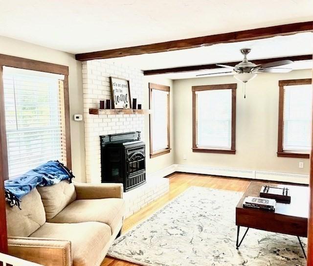 living area with light wood-style flooring, a ceiling fan, baseboards, baseboard heating, and beamed ceiling