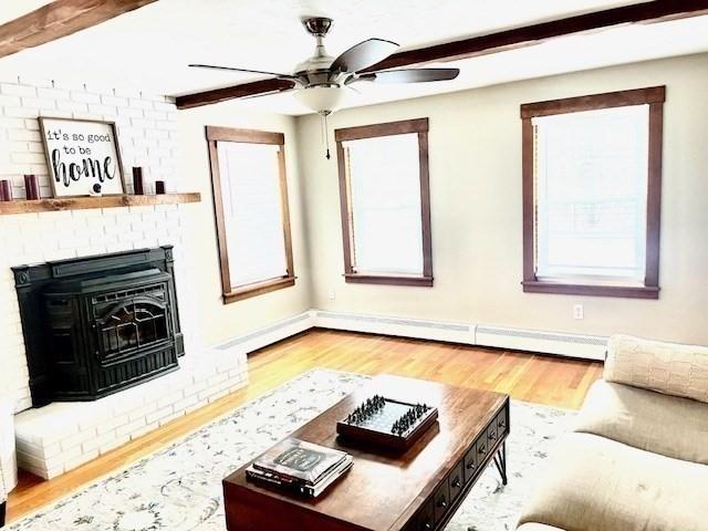 living area with beamed ceiling, a fireplace, wood finished floors, and a ceiling fan