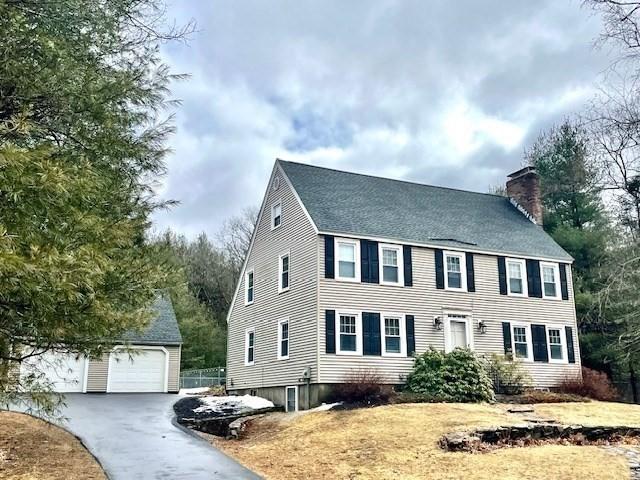 colonial-style house featuring a garage, a chimney, and an outbuilding