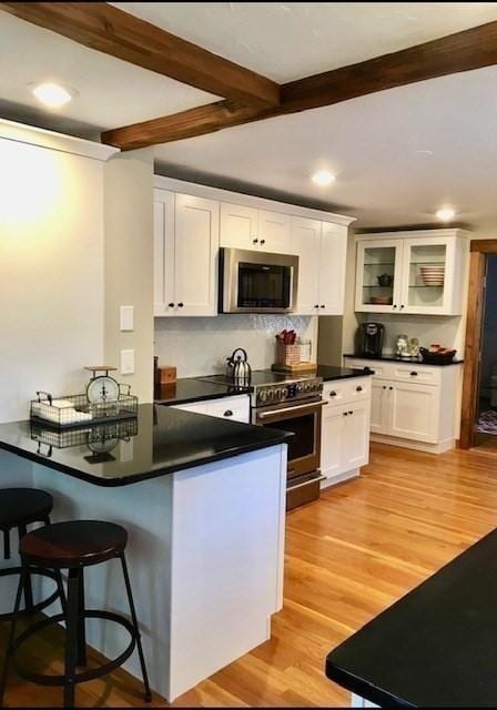 kitchen with light wood-style flooring, white cabinetry, a kitchen breakfast bar, appliances with stainless steel finishes, and dark countertops