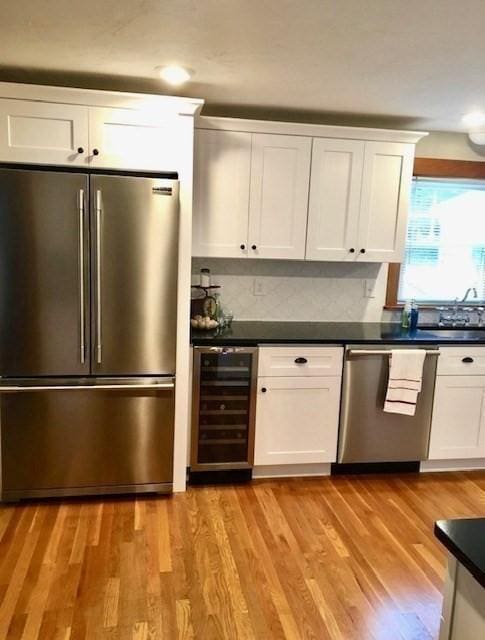 kitchen featuring beverage cooler, white cabinets, appliances with stainless steel finishes, light wood-type flooring, and dark countertops