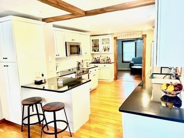 kitchen with a breakfast bar, dark countertops, stainless steel microwave, and light wood finished floors