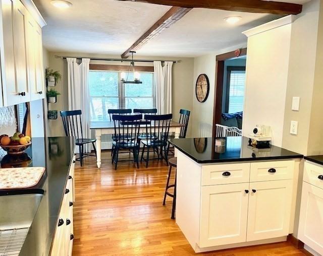 kitchen featuring dark countertops, light wood-style flooring, a peninsula, white cabinetry, and pendant lighting