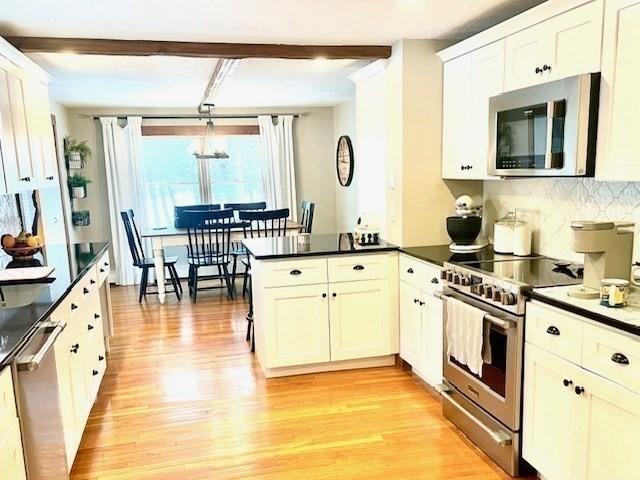 kitchen featuring stainless steel appliances, a peninsula, light wood-style floors, beam ceiling, and dark countertops