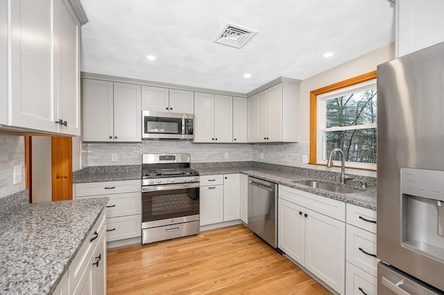 kitchen featuring tasteful backsplash, sink, light hardwood / wood-style floors, stainless steel appliances, and light stone countertops