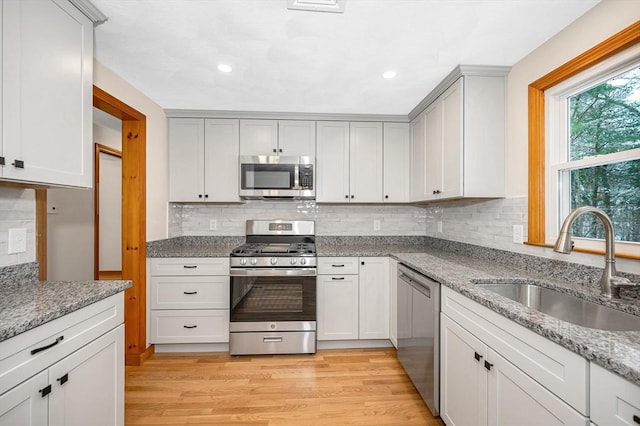 kitchen featuring sink, appliances with stainless steel finishes, tasteful backsplash, light stone countertops, and light hardwood / wood-style floors