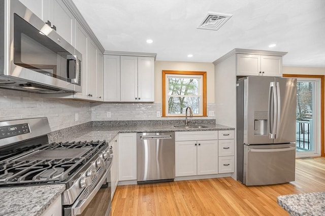 kitchen with sink, light hardwood / wood-style flooring, stainless steel appliances, light stone countertops, and backsplash