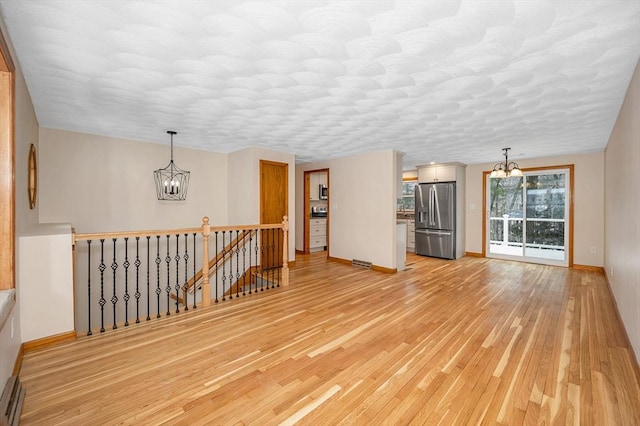 unfurnished living room featuring a chandelier and light hardwood / wood-style floors