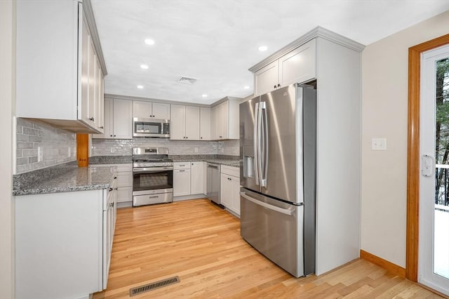 kitchen featuring appliances with stainless steel finishes, tasteful backsplash, white cabinets, light stone counters, and light wood-type flooring