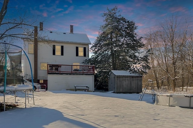 snow covered house with a storage shed, a deck, and a trampoline