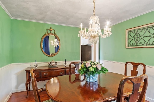 dining area featuring a chandelier, a wainscoted wall, wood finished floors, and crown molding