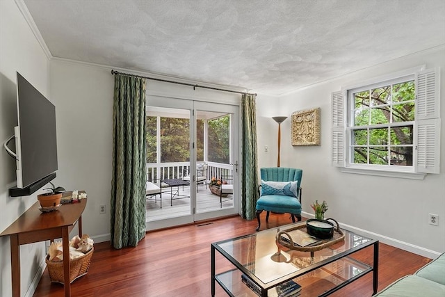 sitting room featuring plenty of natural light, ornamental molding, wood finished floors, baseboards, and a textured ceiling