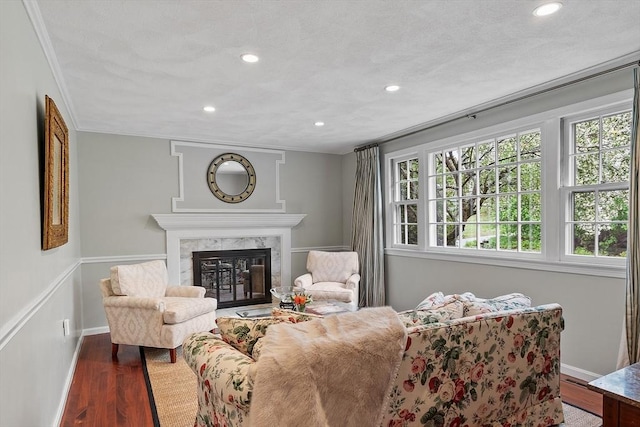 living area with recessed lighting, wood finished floors, ornamental molding, a high end fireplace, and baseboards