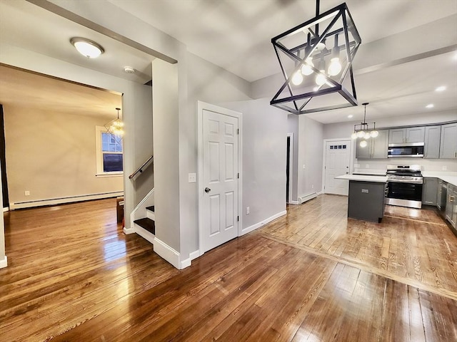 kitchen with gray cabinetry, a baseboard radiator, wood-type flooring, a kitchen island, and appliances with stainless steel finishes