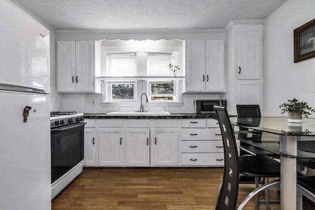 kitchen with freestanding refrigerator, gas range oven, a sink, white cabinets, and dark wood finished floors