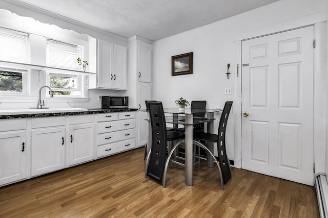 kitchen with stainless steel microwave, a sink, white cabinetry, and wood finished floors