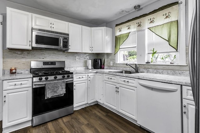 kitchen featuring appliances with stainless steel finishes, a sink, white cabinetry, decorative backsplash, and dark wood-style floors
