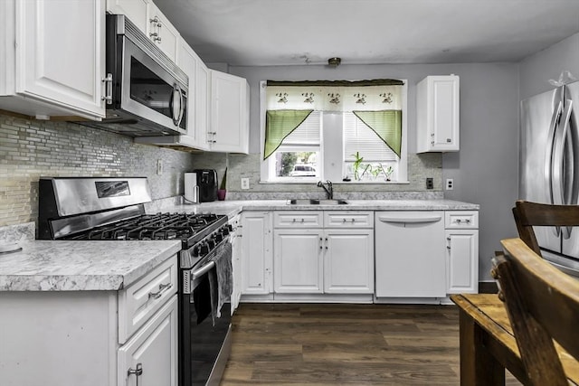 kitchen with appliances with stainless steel finishes, a sink, light countertops, dark wood-style floors, and backsplash