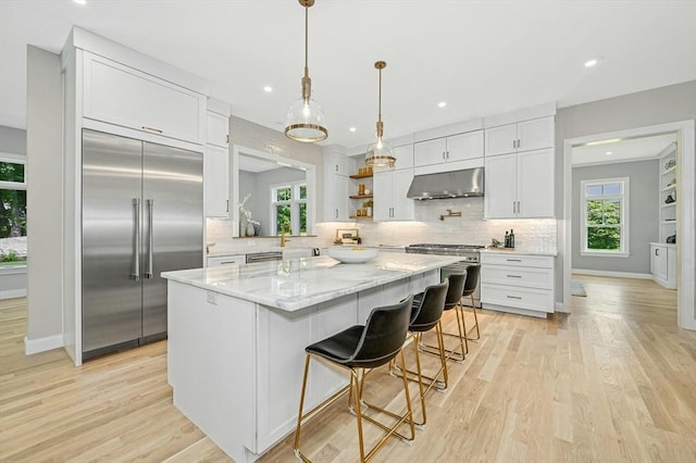 kitchen featuring white cabinetry, a center island, a breakfast bar, exhaust hood, and high end appliances