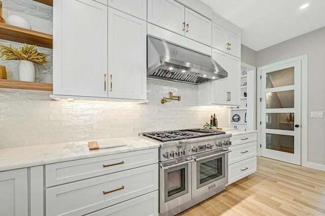 kitchen with white cabinetry, light stone countertops, double oven range, extractor fan, and decorative backsplash