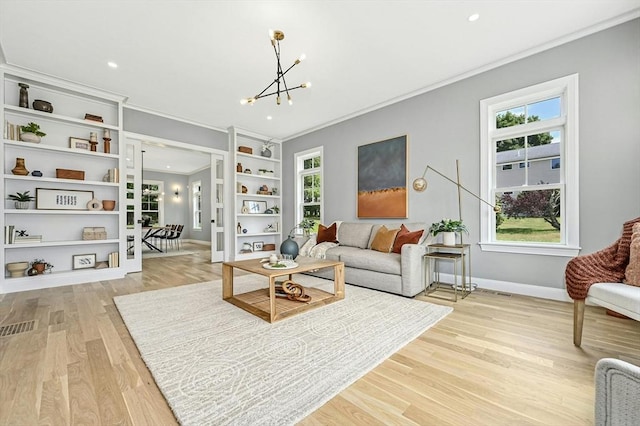 living room with built in shelves, light hardwood / wood-style floors, a notable chandelier, and ornamental molding