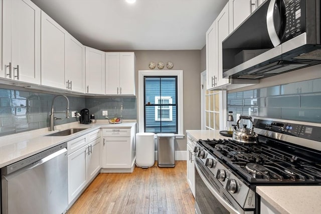 30 Howard St, Cambridge, MA 02139 - kitchen with appliances with stainless steel finishes, a sink, light wood-type flooring, backsplash, and white cabinets