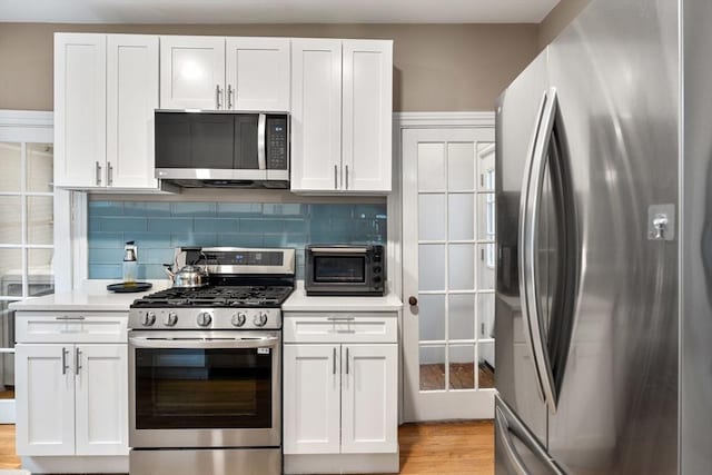 30 Howard St, Cambridge, MA 02139 - kitchen featuring appliances with stainless steel finishes, light countertops, white cabinetry, decorative backsplash, and light wood finished floors