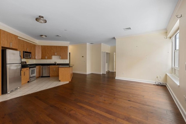 kitchen with a sink, open floor plan, appliances with stainless steel finishes, brown cabinets, and dark countertops