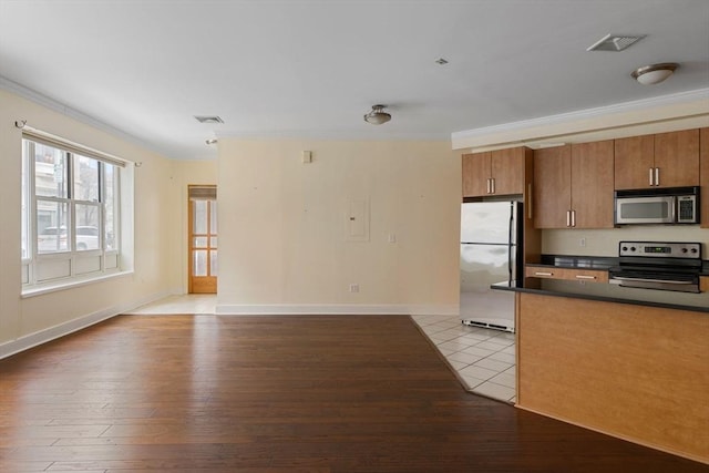 kitchen with stainless steel appliances, dark countertops, ornamental molding, and light wood finished floors