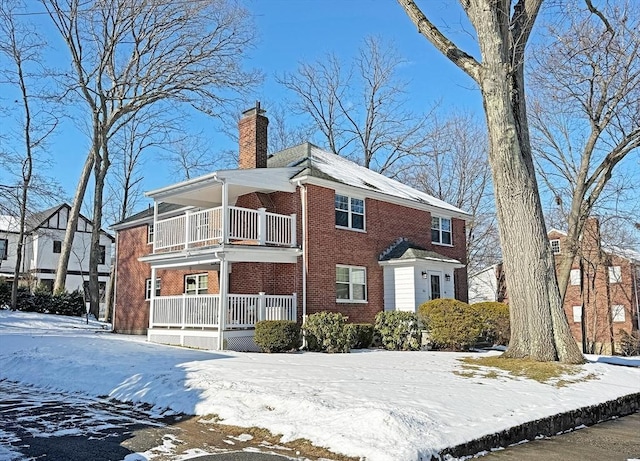 view of front of house featuring a chimney, brick siding, and a balcony