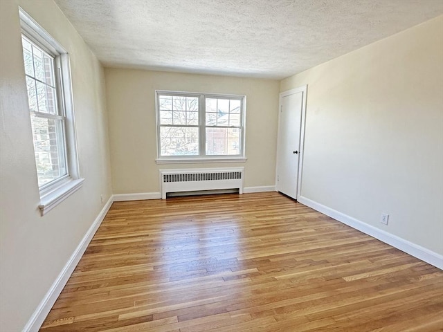 spare room featuring a textured ceiling, light wood finished floors, radiator heating unit, and baseboards