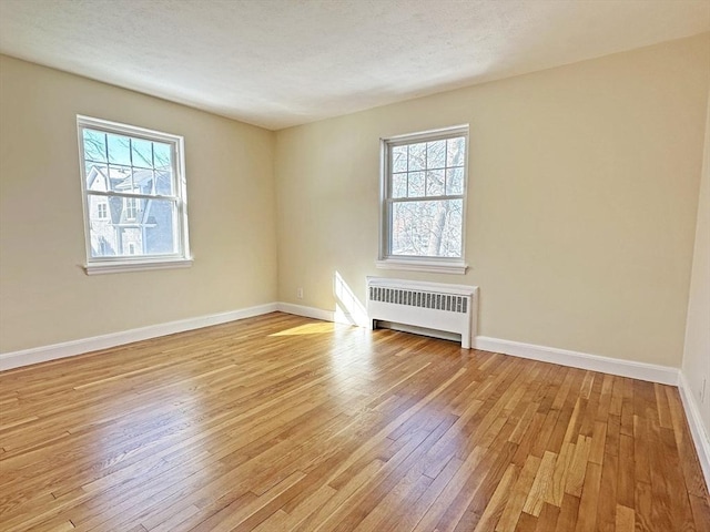 unfurnished room featuring light wood-type flooring, radiator, a textured ceiling, and baseboards