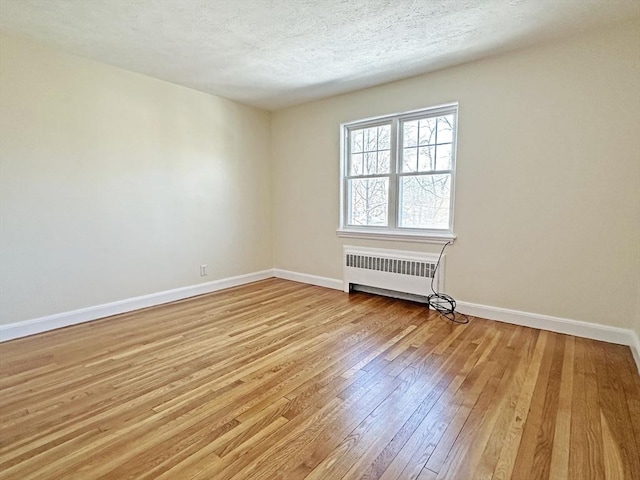 unfurnished room featuring baseboards, radiator heating unit, a textured ceiling, and light wood-style floors