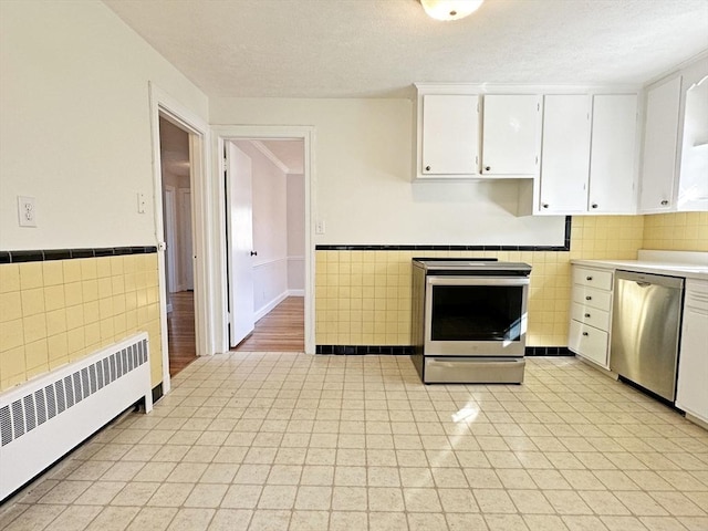 kitchen with white cabinets, appliances with stainless steel finishes, tile walls, and radiator