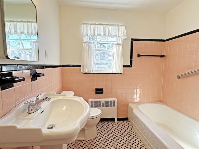 bathroom with a tub to relax in, tile walls, toilet, radiator heating unit, and a sink