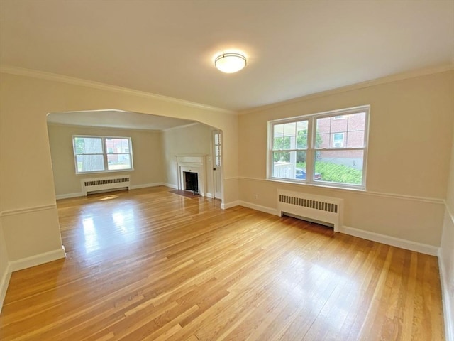 unfurnished living room featuring ornamental molding, radiator heating unit, light wood-type flooring, and a fireplace with flush hearth