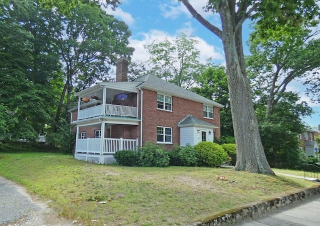 view of front facade with brick siding, a chimney, a front lawn, and a balcony