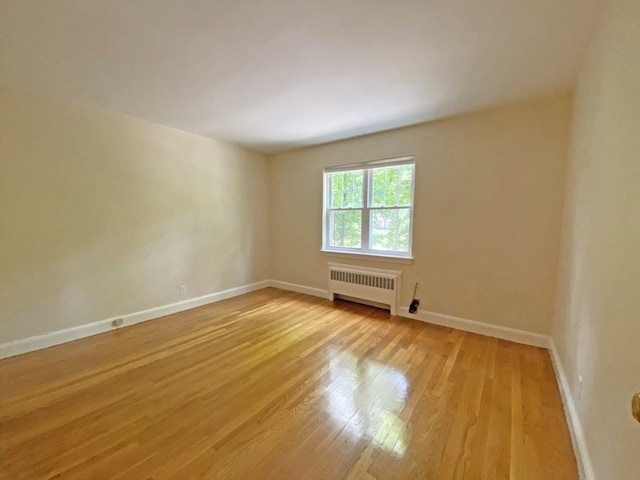 spare room with light wood-type flooring, radiator heating unit, and baseboards