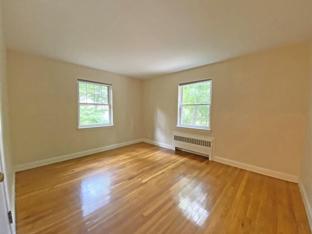 empty room featuring baseboards, a healthy amount of sunlight, wood finished floors, and radiator