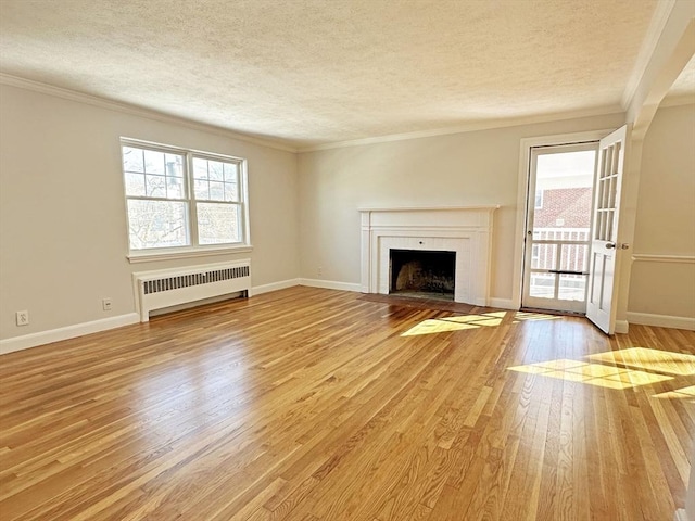 unfurnished living room with a textured ceiling, light wood finished floors, baseboards, and radiator