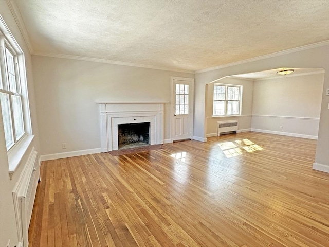 unfurnished living room featuring radiator, light wood-style floors, a fireplace with flush hearth, a textured ceiling, and baseboards