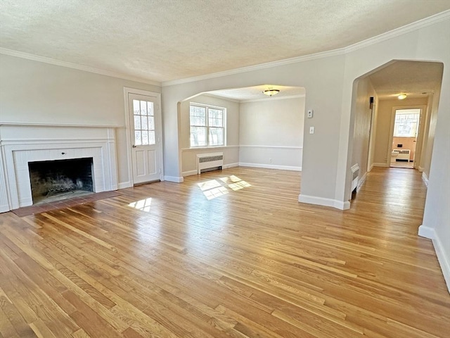 unfurnished living room with arched walkways, a textured ceiling, light wood-type flooring, and radiator