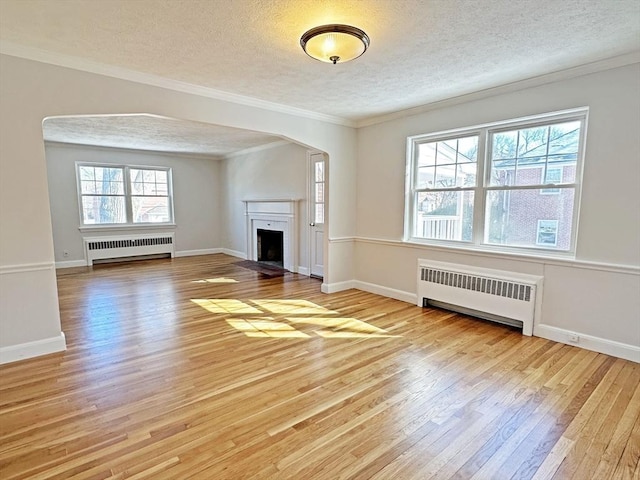 unfurnished living room with a textured ceiling, light wood-style floors, crown molding, and radiator