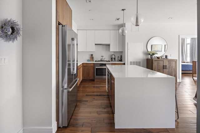 kitchen featuring a kitchen island, hanging light fixtures, dark wood-type flooring, light countertops, and appliances with stainless steel finishes