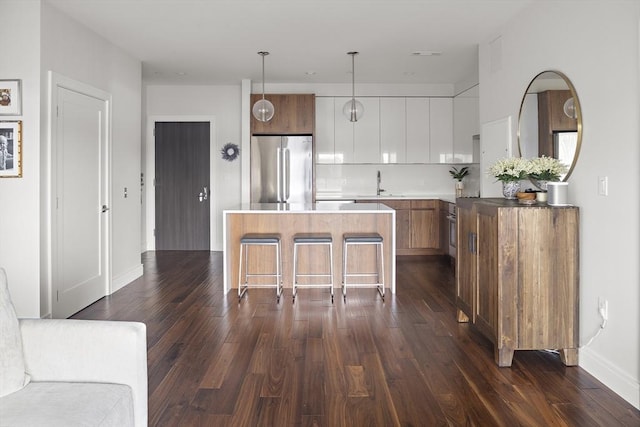 kitchen featuring a kitchen island, dark wood-type flooring, a breakfast bar, stainless steel refrigerator, and a sink