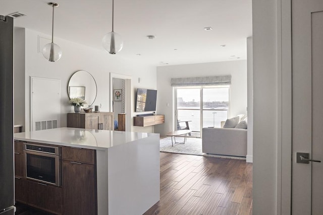 kitchen featuring dark wood-type flooring, light countertops, dark brown cabinetry, stainless steel oven, and open floor plan