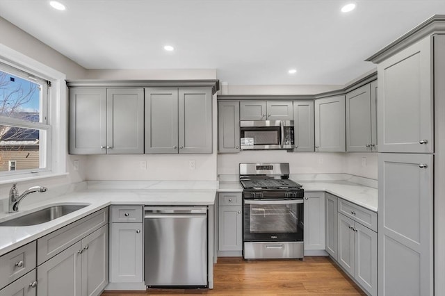 kitchen with stainless steel appliances, light hardwood / wood-style floors, sink, gray cabinets, and light stone counters