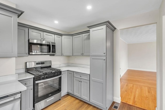 kitchen featuring light wood-type flooring, appliances with stainless steel finishes, gray cabinets, and light stone counters