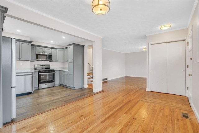 kitchen with appliances with stainless steel finishes, gray cabinets, light wood-type flooring, and ornamental molding